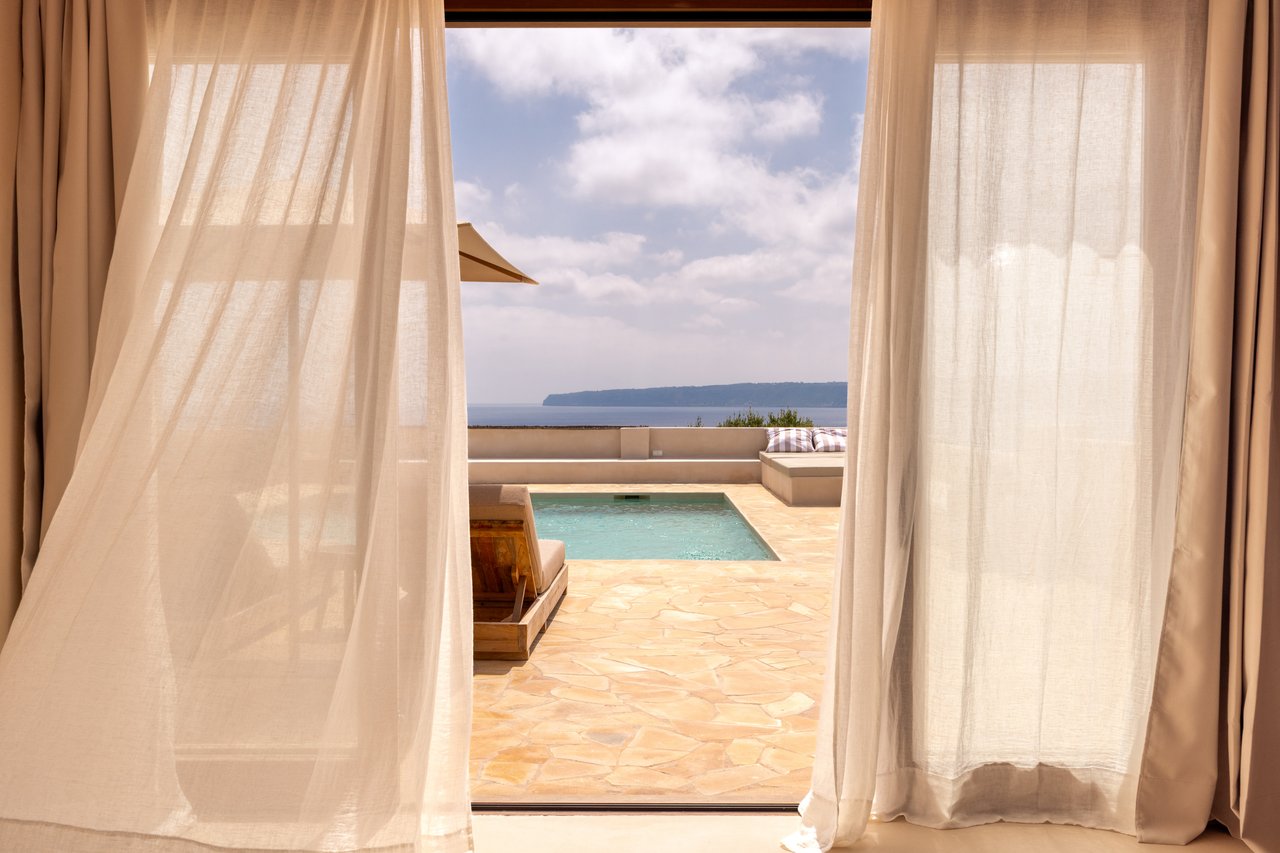 Vista desde la habitación 01 entre cortinas de lino hacia la piscina y el mar