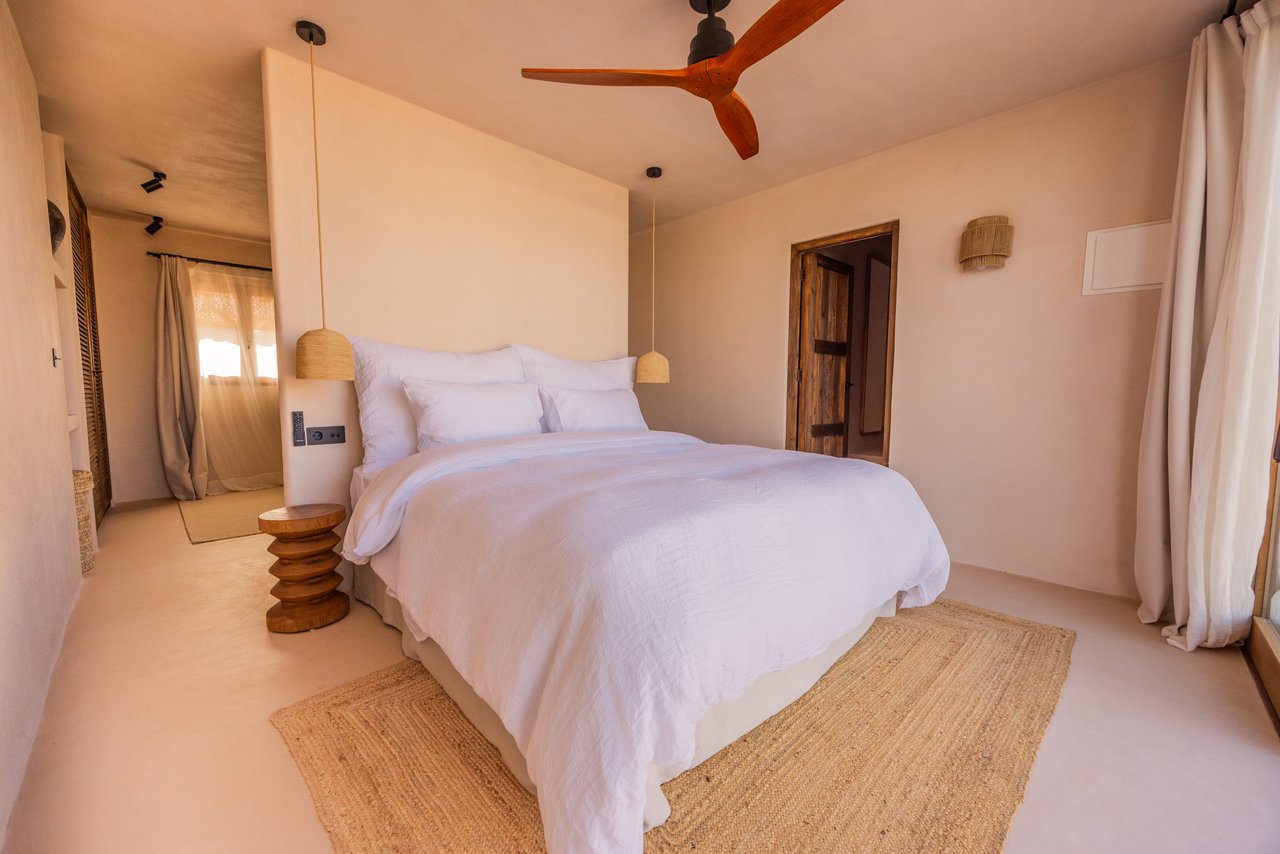Habitación 03: cama blanca, ventilador de madera y alfombra de yute